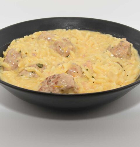 Een kom met een portie sinaasappelorzo met gekruide gehaktballetjes.