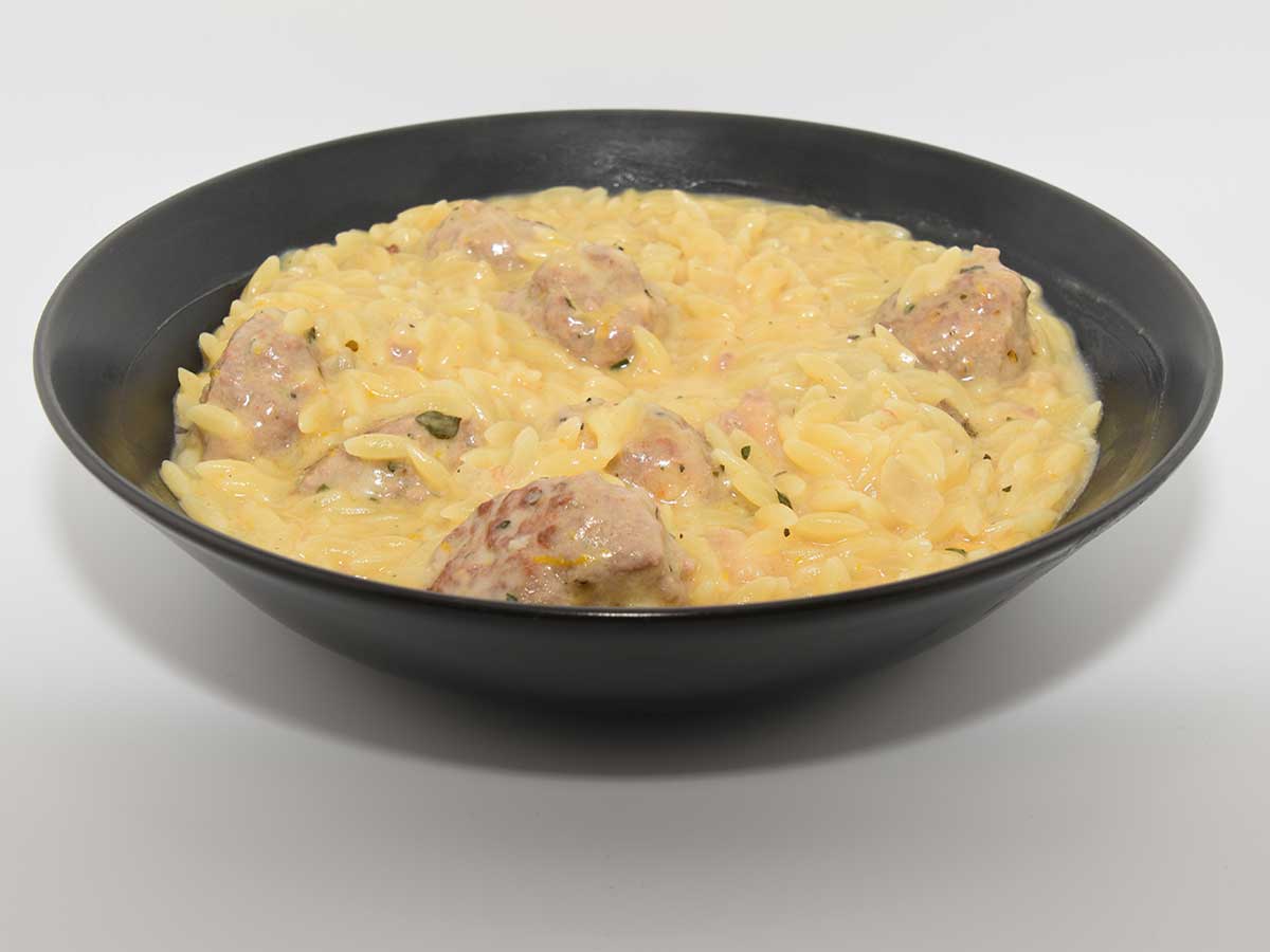 Een kom met een portie sinaasappelorzo met gekruide gehaktballetjes.