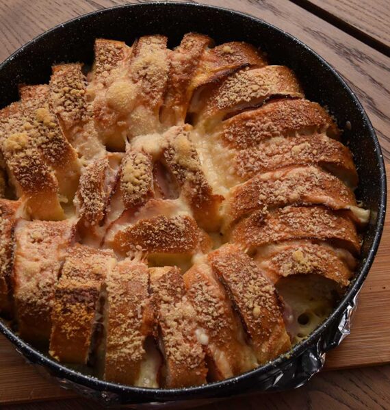 Een rond bakblik met daarin een net gebakken stokbroodring met ham en kaas.