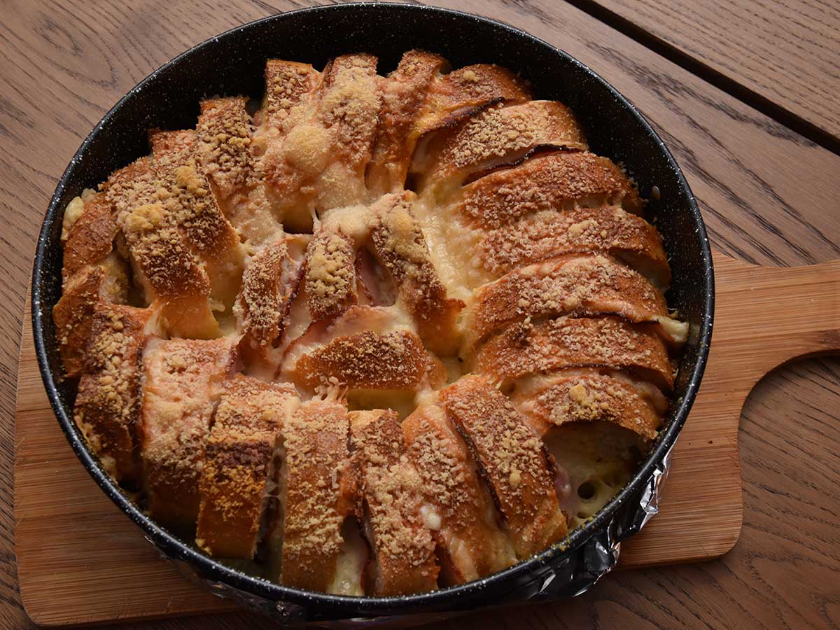 Een rond bakblik met daarin een net gebakken stokbroodring met ham en kaas.