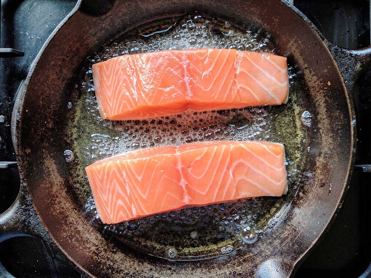 2 op de huid gebakken zalmfilets in een koekenpan.